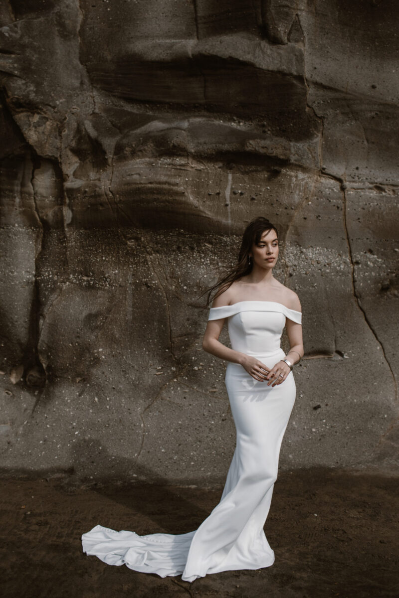 This simple sheath royally-inspired wedding dress with off-the-shoulder straps & straight neckline gives the Kennedy gown a sophisticated look.
