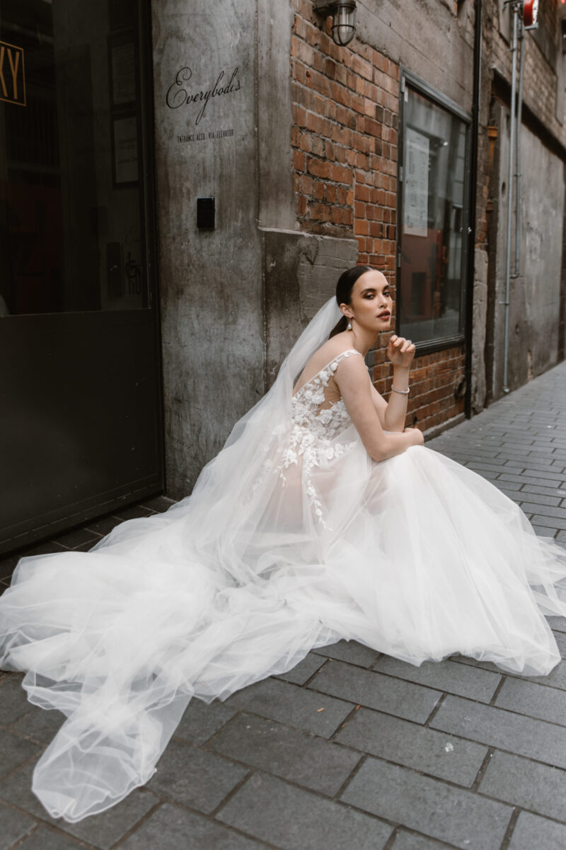 This A-line princess wedding gown has a deep V neck and open back, scattered with delicate 3D flowers that trickle down into the soft tulle skirt.