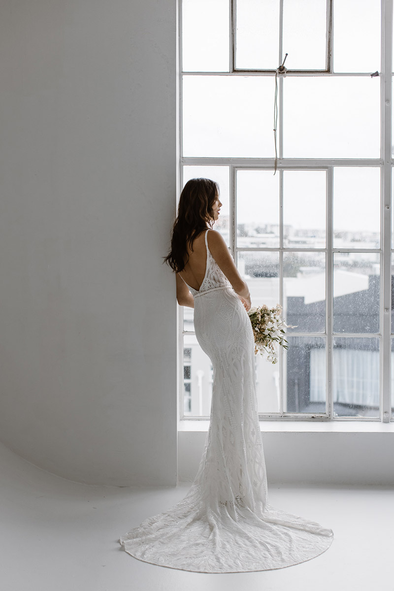 The mermaid off the shoulder silhouette of our Paloma wedding dress enhances your curves with the artful placement of the leafy vine lace applique design.